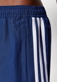 Pantalones cortos deportivos de color navy con una cintura elástica, que presentan tres rayas verticales blancas a lo largo de los lados y una textura de tela suave.