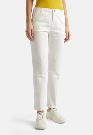 Pantalones de algodón blancos de corte ajustado, con bolsillos frontales, cierre de botón y tobillos rematados, combinados con zapatillas blancas.