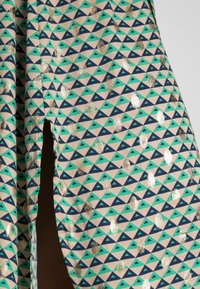 Tessuto a fantasia con un design alternato di triangoli e pois in verde, blu navy e oro su uno sfondo beige chiaro.