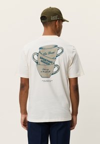 Λευκό βαμβακερό μπλουζάκι με γραφικό στοιχείο στοιβαγμένων φλιτζανιών καφέ, τιρκουάζ κείμενο που αναγράφει "Les Deux" και "SPORTING GOODS", με casual εφαρμογή.