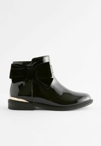 Schwarze lackierte Kunstleder-Ankle-Boots mit einer großen schwarzen Samtschleife auf der Rückseite und einem metallisch goldenen Akzent am Absatz. Flache Sohle.