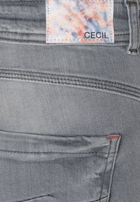 Jean gris de mezclilla con un acabado texturizado, costuras en contraste y una etiqueta de la marca CECIL con un diseño abstracto colorido.