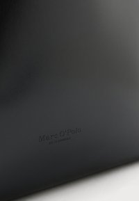 Schwarze Lederbörse mit eingeprägtem "Marc O’Polo"-Logo. Glatte Textur, minimalistisches Design und dezente Markenkennzeichnung.