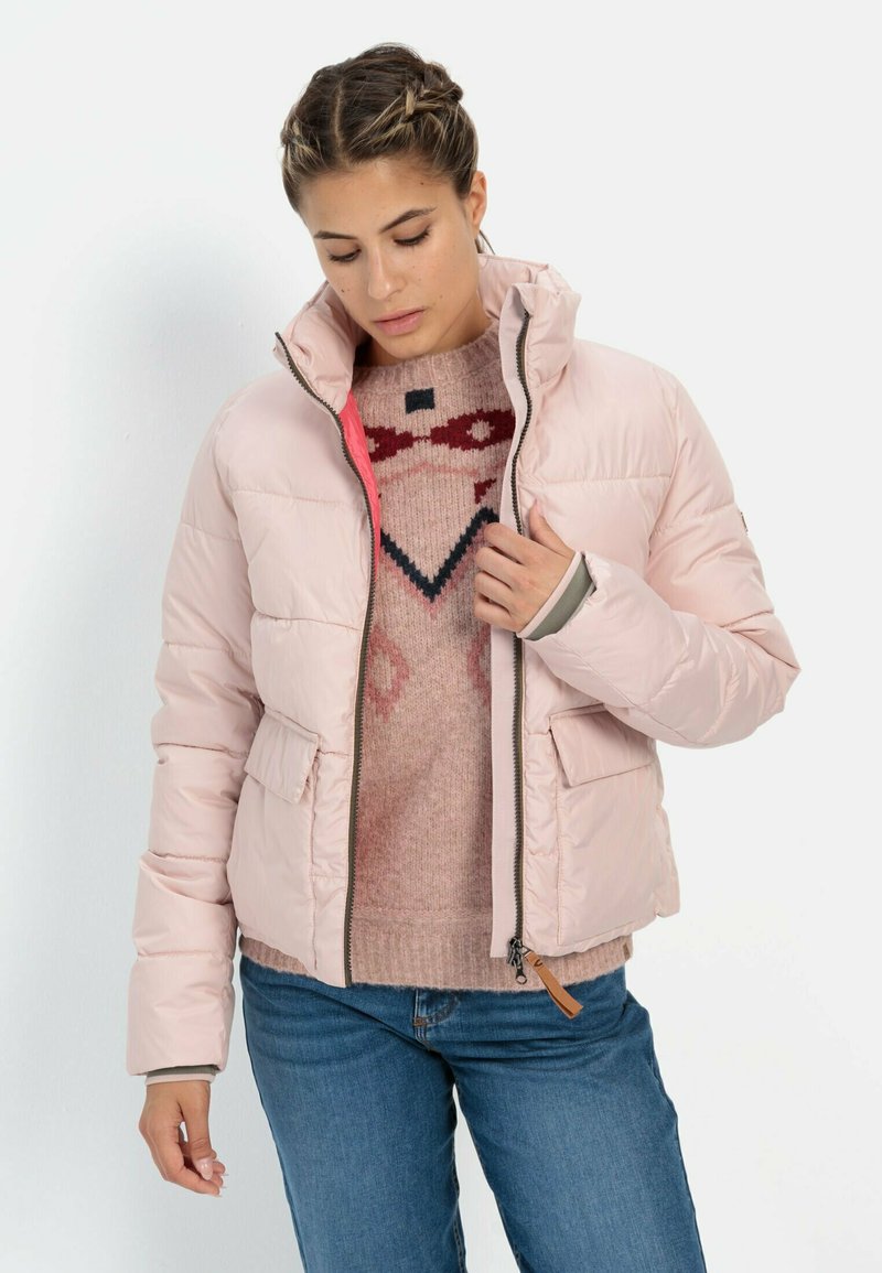 Puffet lyserød jakke med høj krave, lynlåslukning og to frontlommer. Kombineret med en strikket sweater med et geometrisk mønster.