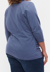 Blå, långärmad topp med rundad halsringning och rynkade detaljer på sidorna. Mjuk, lättviktsfabric; kombinerad med mörk denim.