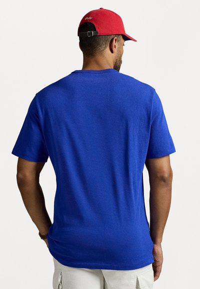 Μπλε κοντομάνικο μπλουζάκι με στρογγυλή λαιμόκοψη, κατασκευασμένο από κράμα βαμβακιού. Κόκκινο καπέλο του μπέιζμπολ με ρυθμιζόμενο λουράκι, με λογότυπο στο πίσω μέρος.