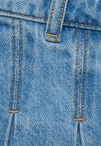 Hellblauer Denim-Stoff mit orangefarbenen Nähten, ausgestattet mit einem Taillenbund und kleinen Falten. Die Textur ist glatt mit einem leicht verwaschenen Erscheinungsbild.