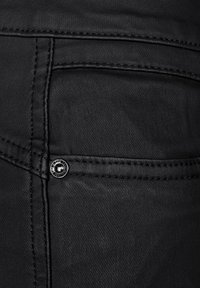 Black denim fabric features a pocket with a silver button and contrasting black stitching. The overall texture appears smooth with a slight sheen.