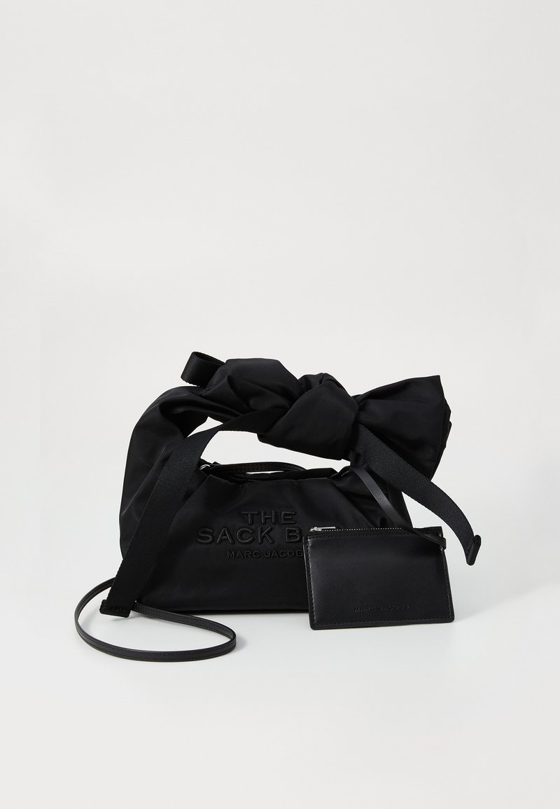 Saco tipo balde em nylon preto com alças superiores com nó, logotipo em relevo e um porta-cartões em pele preta destacável. Textura suave e design minimalista.