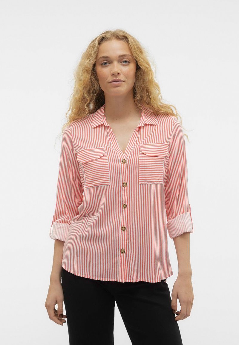 Chemise rayée rouge et blanche avec un devant à boutons, deux poches poitrine, manches longues retroussées aux coudes et coupe décontractée. Texture de tissu douce.