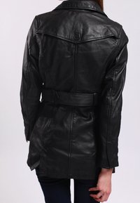 Černý kožený trenčkot s opaskem v pase, výstřihovým límcem a zády s yoke, se šitými detaily a bočními rozparky.