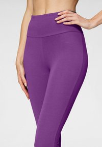 Prilagođene ljubičaste tajice s visokim strukom, izrađene od glatkog materijala. Imaju široku waistband i bešavne strane za udobnost.