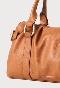 Braune Lederhandtasche mit geraffter Textur, einem goldfarbenen Hardware-Ring und einer Schnallen-Detail auf einem flachen Riemen. Verfügt über eine weiche, glatte Oberfläche.