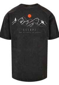 Zwarte katoenen t-shirt met een bergafbeelding en een oranje zon, het woord "ESCAPE" en "EN ONTDEK DE WERELD" in witte tekst.