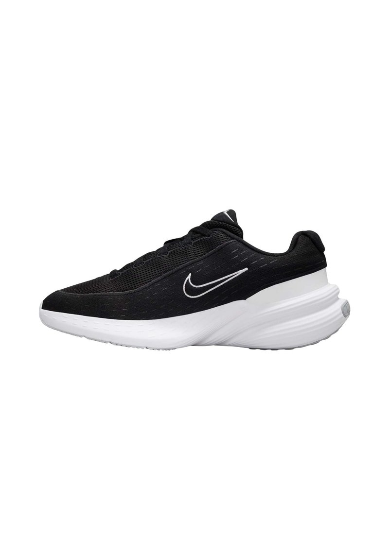 Zapatillas deportivas negras con parte superior de malla, suela blanca y un prominente logo de swoosh. Presentan una forma redondeada y acentos texturizados en la parte superior.