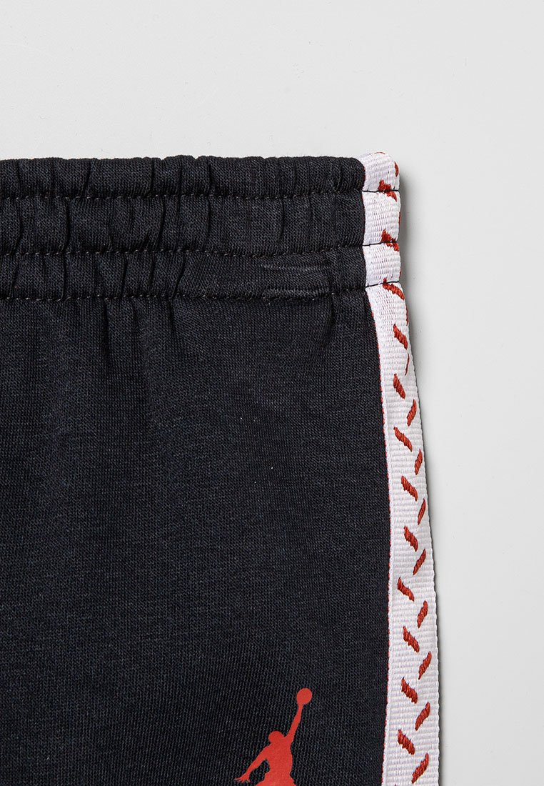 Pantaloni della tuta neri con vita elastica, rifiniture laterali bianche con cuciture rosse, e un logo rosso sulla gamba sinistra.