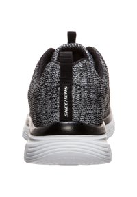 Le scarpe sportive nere e grigie presentano una parte superiore in rete testurizzata, un controcuscino nero e una suola in gomma bianca con scanalature orizzontali.
