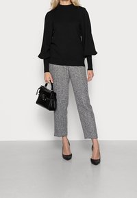 Zwarte gebreide trui met opgeblazen mouwen, grijs-witte patroonbroek en een zwarte handtas met krokodillenprint. Zwarte pumps met spitse neus.