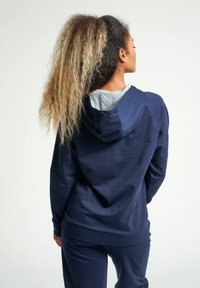 Felpa blu navy con interno grigio, dotata di orlo e polsini a costine. Tessuto morbido e cappuccio con coulisse. Vestibilità casual abbinata a pantaloni.