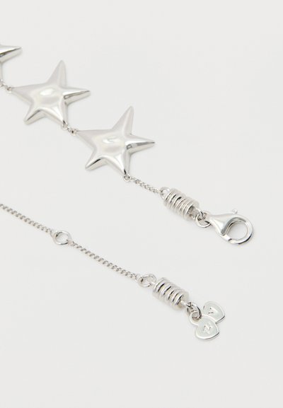 Strieborný reťazec v tvare hviezdy so sponou typu langusta a malými srdcovými príveskami s vygravírovanými písmenami na bielom pozadí.