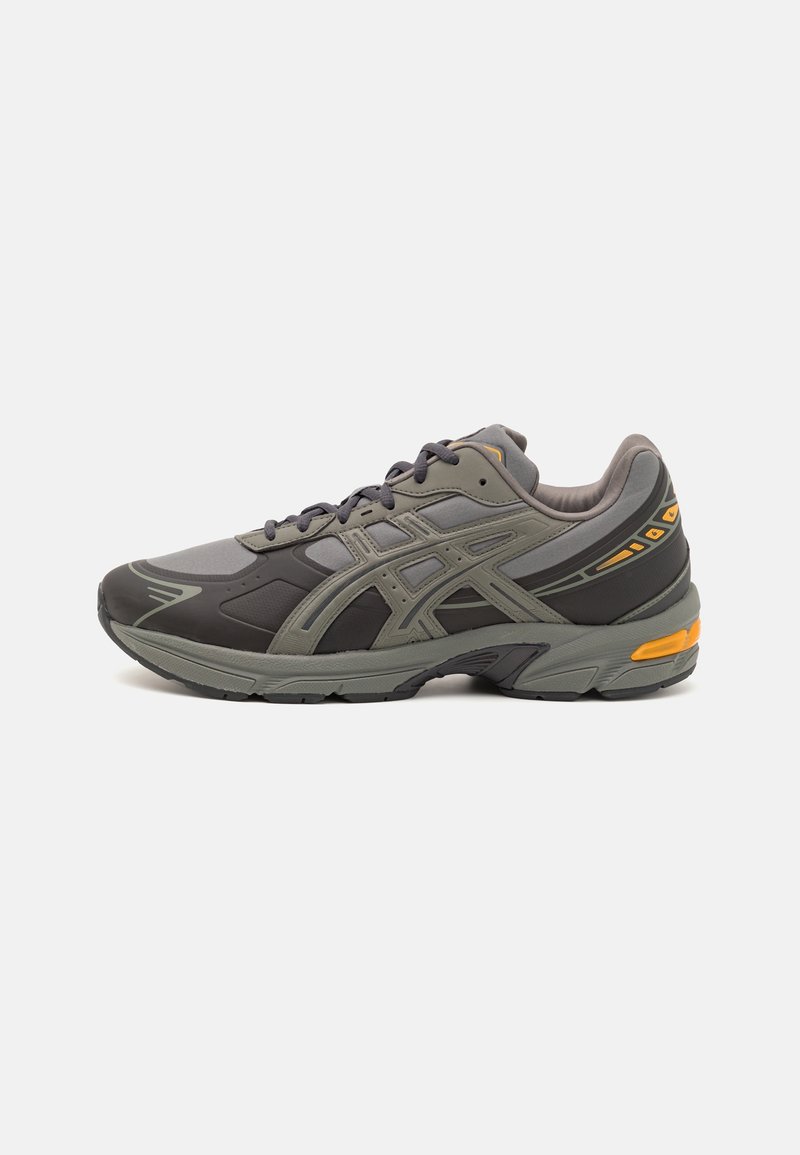 Chaussure de sport gris foncé et olive avec semelle noire, laçage à l'avant, et accents orange sur le talon et la languette, vue latérale sur fond blanc.