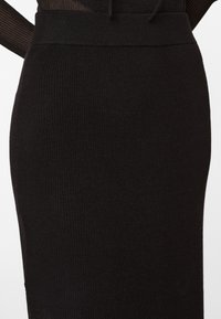 Jupe crayon en tricot côtelé noir avec une taille large et une texture lisse, mettant en valeur une silhouette ajustée.