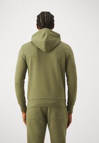 Sudadera verde oliva con capucha ajustable, puños de punto ribeteado y bolsillo tipo canguro. Tejido suave con una textura lisa y un corte casual.