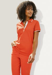 Korte mouw polo shirt in feloranje met een witte knoopsluiting en kraagaccenten, gecombineerd met bijpassende aansluitende broeken. Zachte textuur.