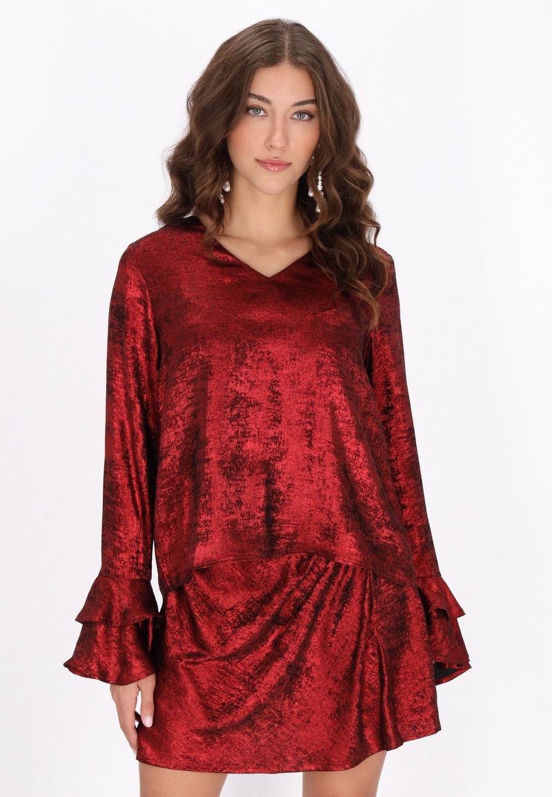 Rød, skinnende, fløjlsagtig kjole med lange ærmer. V-halsudskæring og flæsekantede manchetter. Draperet stil med løs pasform og tekstureret stof.