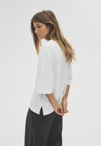 Biała, oversize koszulka z krótkim rękawem, z bocznym rozporkiem, w połączeniu z ciemnymi spodniami w prążki. Gładki, bawełniany materiał.