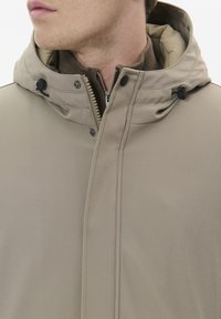 Beige jacka med dragkedja framtill och huva, med en texturerad innerfoder, justerbara dragsnöre och tryckknappar. Slät tygyta.
