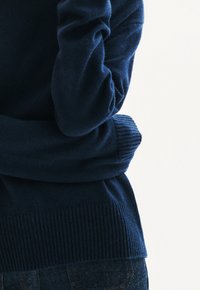 Maglione lavorato a maglia blu navy con polsini e orlo ribattuti, caratterizzato da una finitura morbida e testurizzata. Sono visibili dettagli ravvicinati del tessuto.