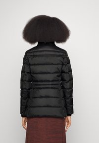 Veste rembourrée noire avec un col haut, un design gonflé et une taille ajustée. Texture lisse et manches longues, vue de dos.