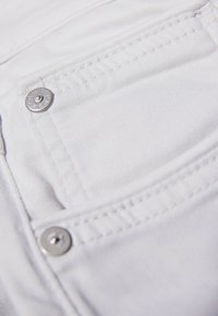 White fabric of a jeans pocket with visible stitching, a metal button, and a smooth texture, featuring a clean and minimalist design.