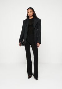 Mustas ülikond, millel on kohandatud bleiser ja kitsad püksid, lisaks läbipaistev must topp. Aksessuaaride hulka kuulub väike must käekott ja terava esisega kingad.