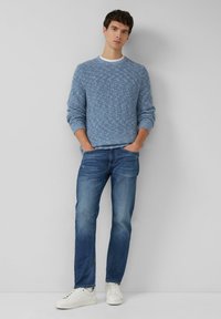 Hellblauer gestrickter Pullover mit strukturierter Optik, kombiniert mit mittelblauen Jeans und weißen Sneakern. Lässige Passform und mehrlagiges Design.