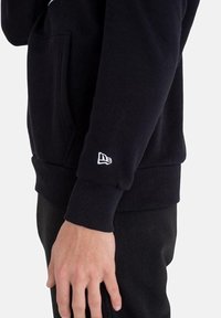 Felpa nera con polsini e orlo a costine, dotata di una tasca frontale. Piccolo logo bianco sulla manica. Tessuto morbido, design casual.