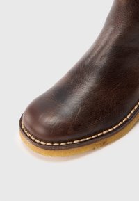 Barna bőrcsizma lekerekített orral, texturált felülettel, bézs cérnával és sárga gumitalppal.