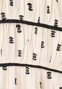 Tela blanca con patrones circulares bordados en negro y plisados verticales, separados por delgadas bandas negras. Textura suave con un detallado intrincado.