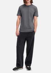 T-shirt corto grigio scuro a maniche corte con scollatura rotonda e dettagli ricamati discreti, abbinato a pantaloni neri larghi e strutturati e sneaker nere.