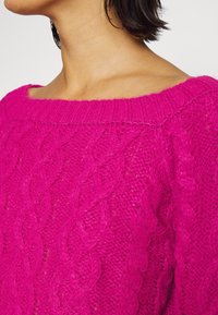 Übergroßer, knallpinkfarbener Strickpullover mit weitem Ausschnitt, der ein strukturiertes Zopf-Design und einen gerippten Kragen aufweist.