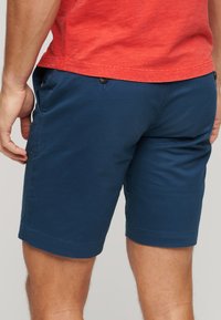 Shorts bleu marine en tissu léger, avec une taille plate, des poches latérales et un détail de bouton unique sur la ceinture.