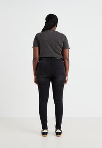 Črne skinny jeans z visokim pasom, dvema zadnjima žepoma in rahlo elastično bombažno mešanico; v kombinaciji s sivo majico s krožnim izrezom.