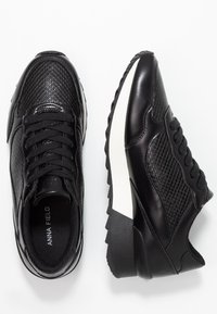 Black sneakers featuring a combination of smooth and textured leather, lace-up design, white midsole, and distinct tread pattern.