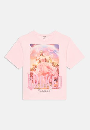Lyserød kortærmet t-shirt med et livligt grafik af en figur i en lyserød kjole, omgivet af bobler og ordet "WICKED" i glitrende lyserød.
