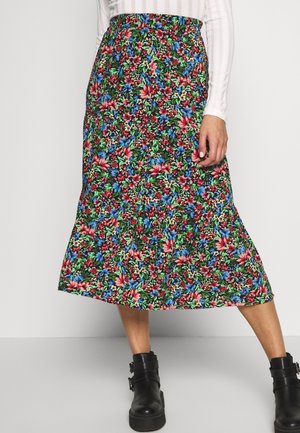 Jupe fleurie mi-longue avec des fleurs rouges, bleues et vertes, associée à des bottines noires et un top blanc à manches longues en maille côtelée.