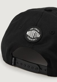 Sapca de baseball neagră cu vizieră plată și sistem de ajustare tip snapback. O plăcuță rotundă din cauciuc negru afișează logo-ul "PALLADIUM 1947".