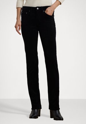 Jeans in velluto nero con design a gamba dritta, dotati di cinque tasche, chiusura con bottone metallico e superficie texturizzata. Indossati con stivali con tacco.