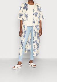 Henkilö, joka pukeutuu vaaleansinisiin kapeisiin farkkuihin, valkoisiin sandaaleihin, kermaiseen t-paitaan ja pitkään kermaiseen kimonoon, jossa on sinisiä kukkakuosisia koristeita.