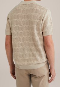 Beige knit polo shirt with honeycomb pattern, short sleeves, ribbed collar and hem. Textured fabric showcases open weave detail.